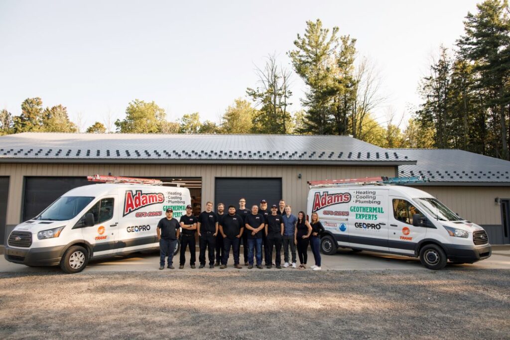 Adams Heating Cooling & Plumbing team in uniforms with service vans parked outside their service facility