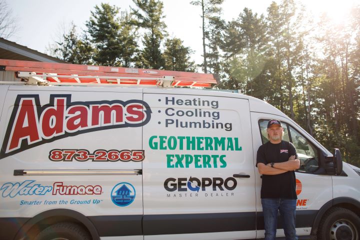 Adams Heating Cooling & Plumbing service technician beside the company’s service van