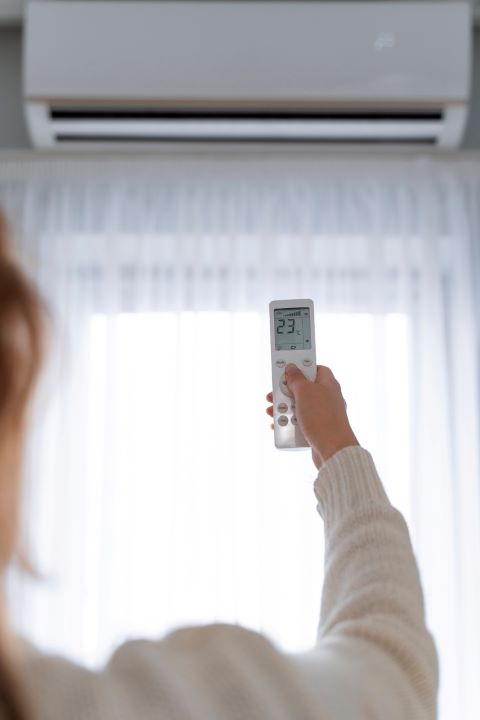 Back view of a woman holding a remote control, turning on the aircon