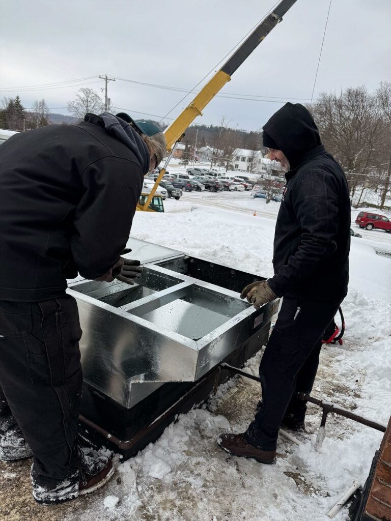 Technicians in snowy outdoor site handling large commercial HVAC unit during installation