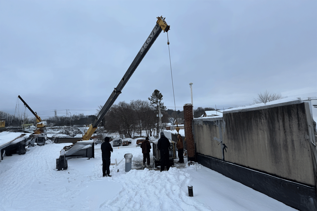 Workers on a snowy day operating heavy equipment and a crane for commercial hvac maintenance work