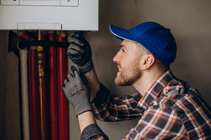 Man in plaid shirt servicing wall-mounted water heater