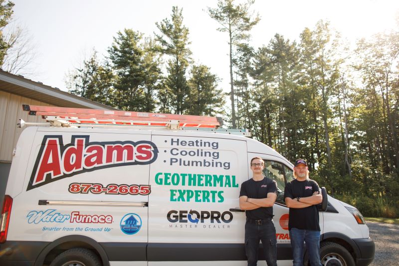 Adams Heating Cooling & Plumbing two technicians standing beside the company’s service van