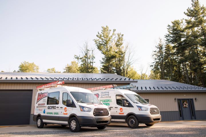 Two Mains service vans of Adams Heating Cooling & Plumbing company parked outside